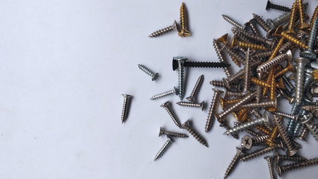 A collection of mixed metal screws, including silver, gold, and black, are scattered across the clean white surface.の写真素材