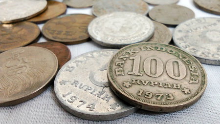 An ancient 100 Rupiah coin from Indonesia from 1973, surrounded by other ancient coins.