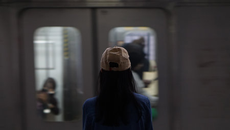 A blurry image of a young woman wearing a beige hat and denim jacket stands on a train platform,...