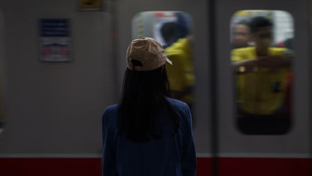 A blurry image of a young woman wearing a beige hat and denim jacket stands on a train platform, watching a train pass by. Jakarta, Indonesia.の写真素材