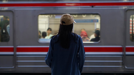 A blurry image of a young woman wearing a beige hat and denim jacket stands on a train platform,...