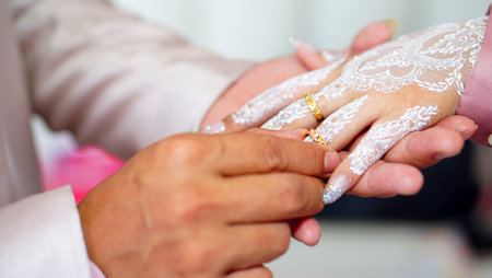 The groom gently places a gold wedding ring on the bride's finger during their wedding ceremony.