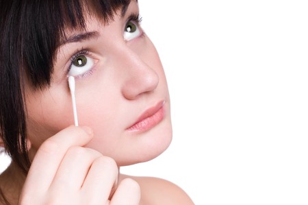 Beautiful young girl removing makeup from eyes with cotton bud isolated on whiteの写真素材