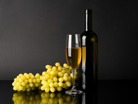 Bottle and glass of white wine with grapes against dark backgroundの写真素材