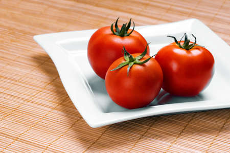 ripe tomatoes on plate on wooden backgroundの写真素材