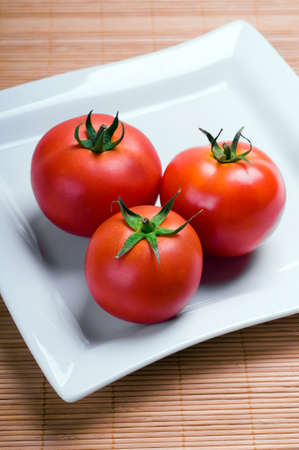 ripe tomatoes on plate on wooden backgroundの写真素材