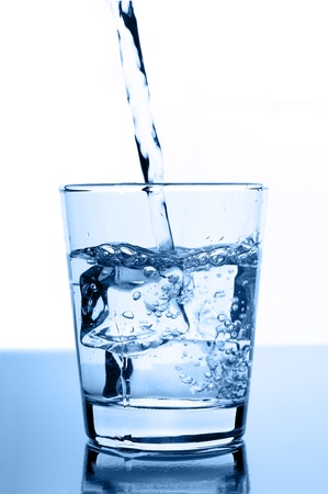 water pouring in to glass with ice cubes on glossy backgroundの写真素材