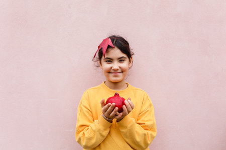 smiling girl holding red pomegranate againts pink wallの写真素材