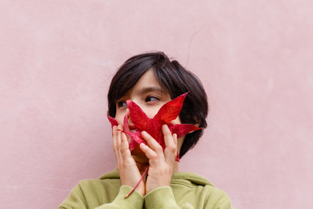 close up of a girl holding big red leaves at her faceの写真素材