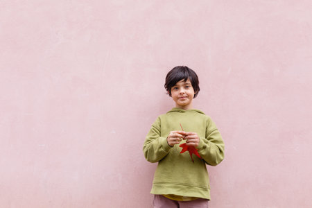 curious child with short hair holding big red leavesの写真素材