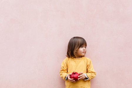 little girl with blond hair holding red pomegranate in her arms