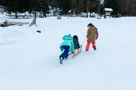 two girls pulling and pushing smaller girl on wooden sled