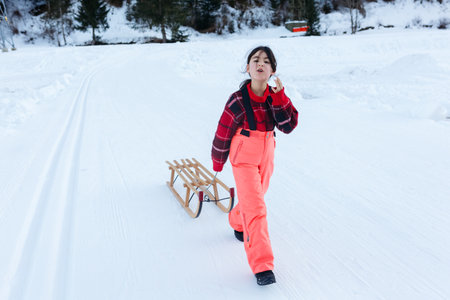 talking girl in red pullover and orange ski pants walking with wooden sledの写真素材