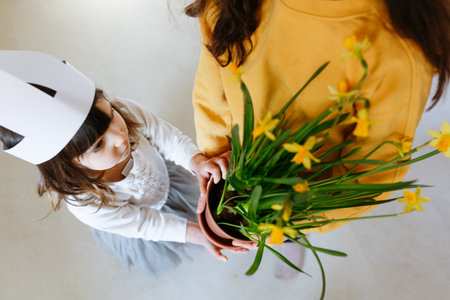 high angle view on two girls with rabbit ears holding pot with daffodils