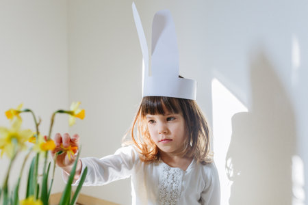 portrait of sad girl with paper ester bunny ears watching daffodil flowers