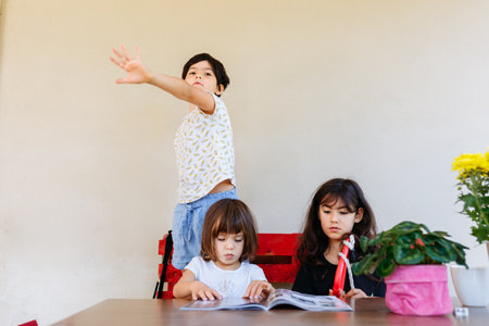 children sitting outside and watching magazine and another child standing and talkingの写真素材
