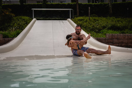 father holding small daughter in hands sliding down in water slide