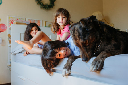 side view on three children sitting on the parents bed and playing with their dogの写真素材