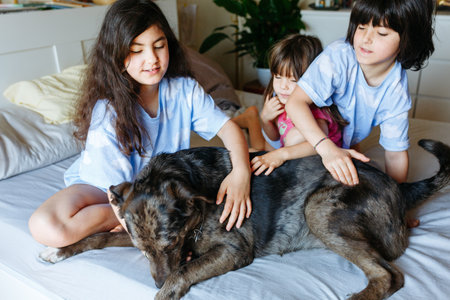 three children sitting on the parents bed and caressing their dogの写真素材