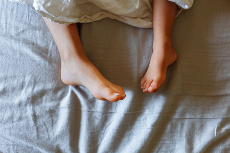 upper view on elder child and smaller child feet in the parents bed under bed sheetの写真素材