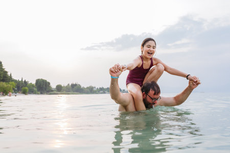 happy girl sitting on the neck of the father standing in the water preparing for a jumpの写真素材