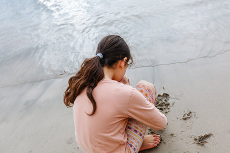 rear view of sitting on the beach girl drawing on the sand next to the seaの写真素材