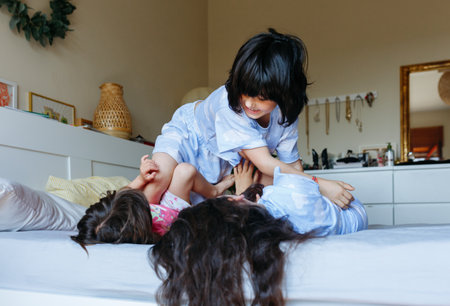 two children lying on the bed and other child jumping overの写真素材