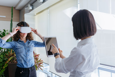 one standing woman in the office using tablet and controlling colleague with VR helmetの写真素材