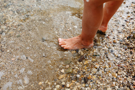 barefeet child legs standing in the water in pebbles beach