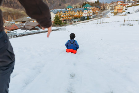 wide angle view of parent helping child with short dark hair to slide down the snowy hillの写真素材
