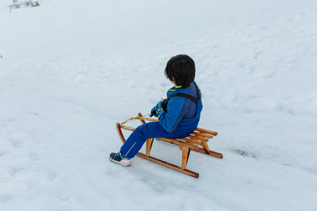child with dark short hair going down snowy hill on wooden sledの写真素材