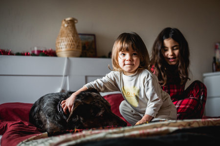 two children in pajamas playing with the dog in the bedの写真素材