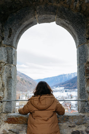 rear view of standing girl watching snowy mountains from the big window