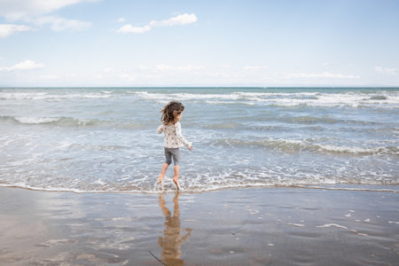 rear view of little girl jumping on the waves at the seasideの写真素材