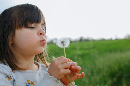 Child blowing a dandelion outside in a green field