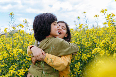 two happy girls hugging each other and laughing in the field with yellow flowers