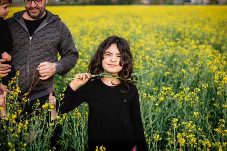 portrait of a smiling girl standing in front of her father with other siblings amidst yellow flowersの写真素材