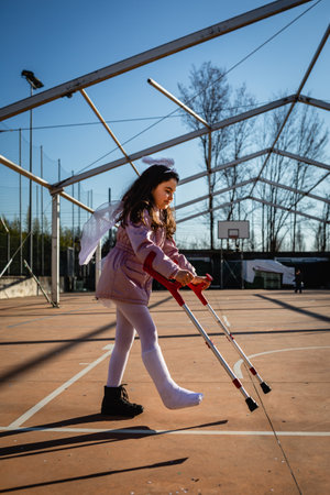 girl with leg in plaster holding crutches wearing angel carnival costume
