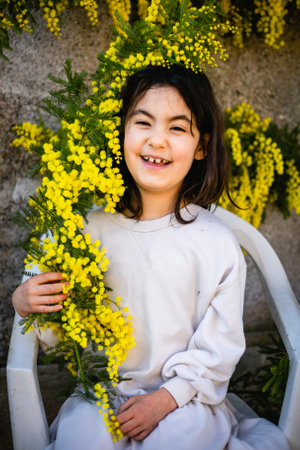 waist up portrait of laughing girl in white dress sitting under with mimosa treeの写真素材