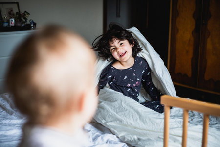 two small children sisters playing on the parents bedの写真素材