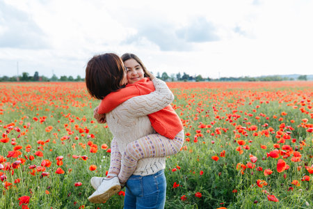 mother holding a daughter in arms in a field full of poppies flowersの写真素材