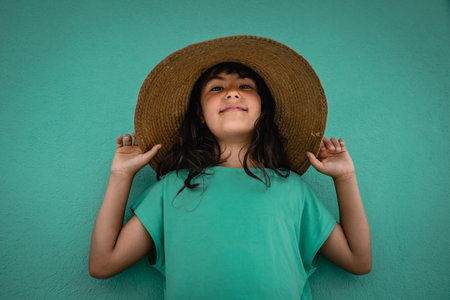 portrait of girl in green t-shirt and straw hat against green wallの写真素材