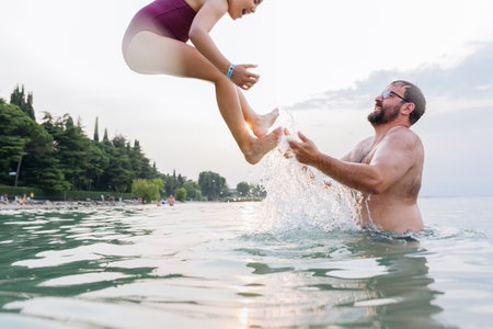 happy girl jumping in the water from the father armsの写真素材