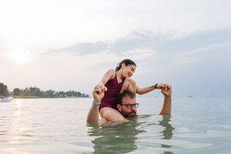 smiling girl sitting on the neck of the father standing in the water preparing for a jump having fun
