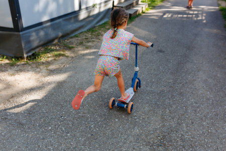 rear view of riding push scooter little girl on a sunny day