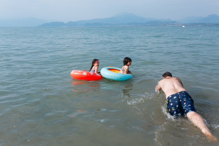 two children having fun in the water swimming in the inflatable rings with the father