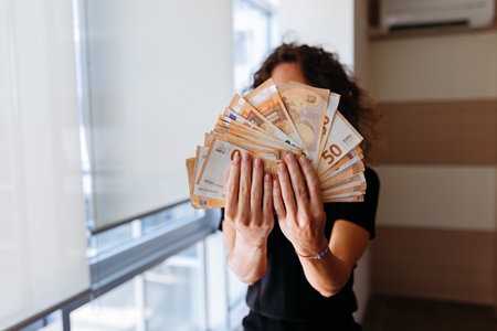 standing in the room woman holding the money with both hands in front of her faceの写真素材