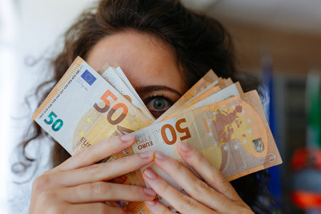 portrait of woman peeking behind money cash looking at cameraの写真素材