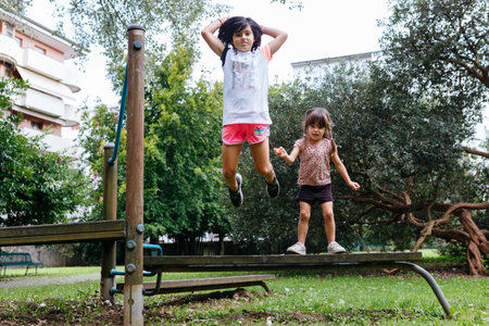 two children jumping from the wooden bench in the park