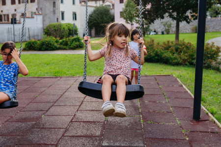 three children playing with swings in public parkの写真素材